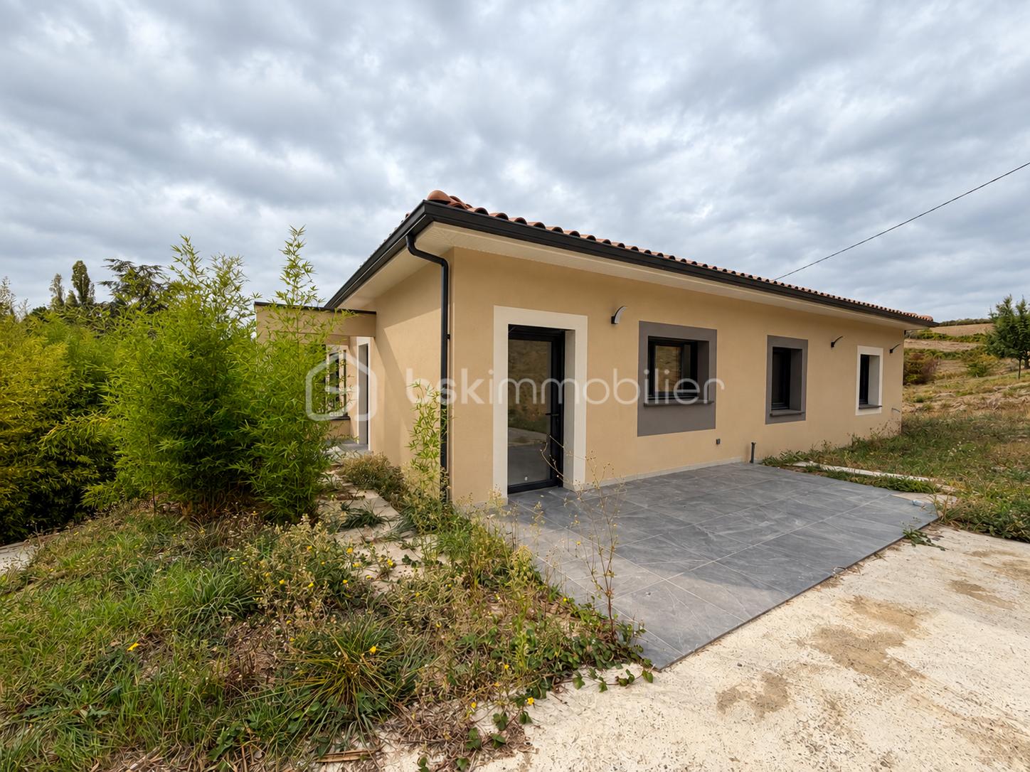 Maison moderne beige sous ciel nuageux.png