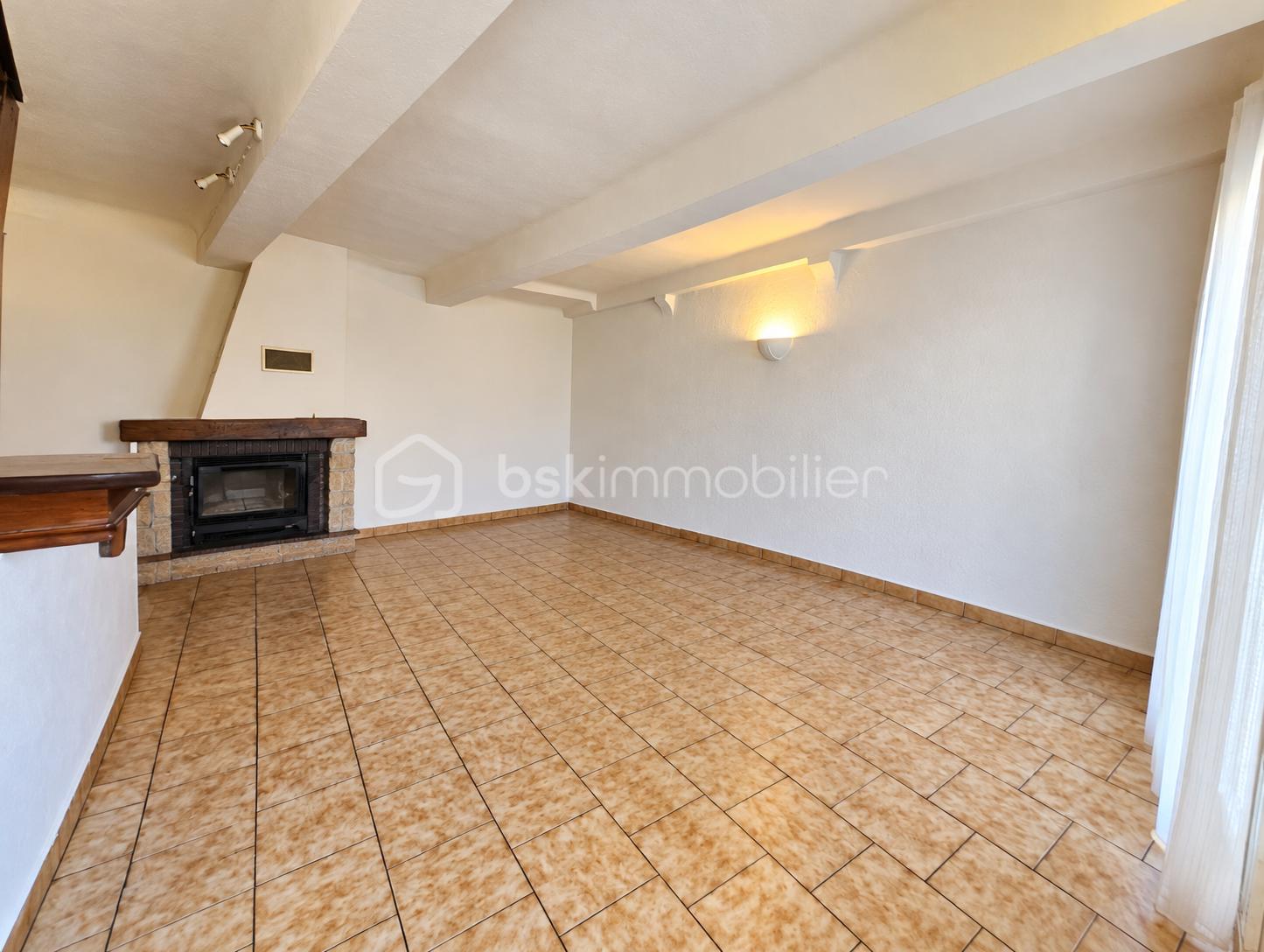 Salon lumineux vide avec cheminée et poutres.png