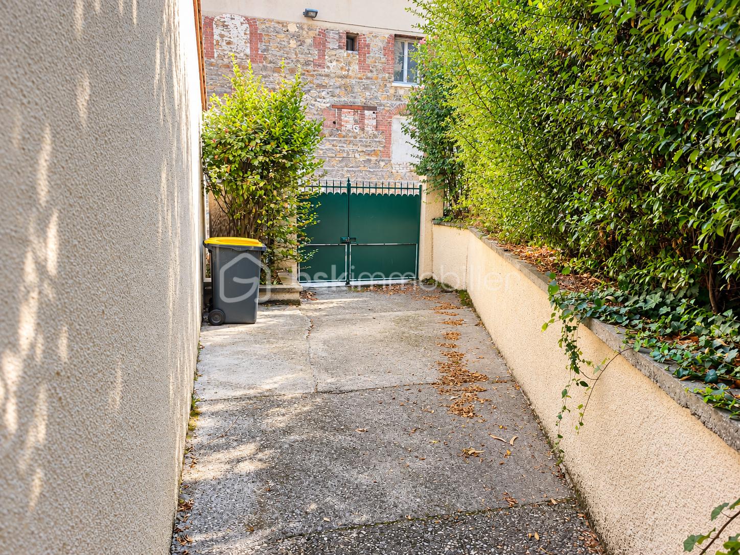 Cour ensoleillée, portail vert et végétation.png